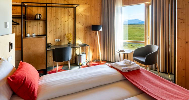 Una habitación de hotel moderna y luminosa con una cama bien arreglada y vistas panorámicas del paisaje rural con las montañas islandesas a lo lejos.