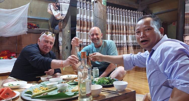 Een groep mannen die op de vloer zitten en samen genieten van een maaltijd en drankjes.