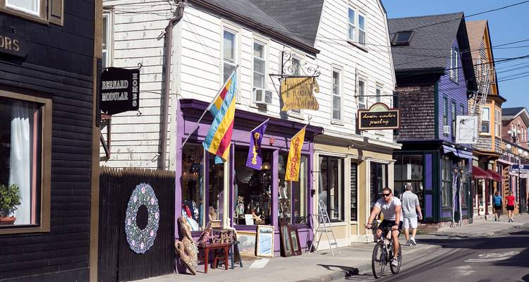 Une rue pittoresque bordée de petites boutiques colorées et de cyclistes sous une lumière matinale éclatante.