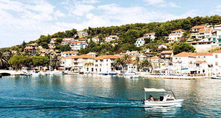 Pueblito tranquilo en la bahía con casas blancas y palmeras reflejadas en aguas azules mientras una pequeña lancha motora deja su estela.