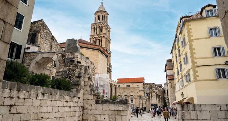 Los peatones exploran el Peristilo de Split con la torre campanario de San Dominio elevándose sobre las ruinas de piedra antigua.