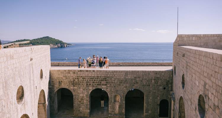Un pequeño grupo de turismo se encuentra en la parte superior de las enormes murallas de la fortaleza de Dubrovnik mirando hacia el horizonte del Mar Adriático.