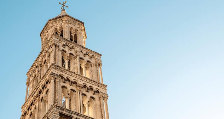 Primer plano de la torre campanario románica de Split iluminada contra un cielo azul despejado.