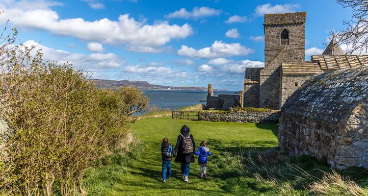 Una familia caminando hacia un antiguo edificio de piedra junto al mar.