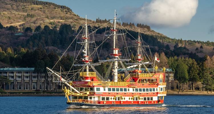 Buntes historisches Schiff segelt auf einem See mit Bäumen im Hintergrund.