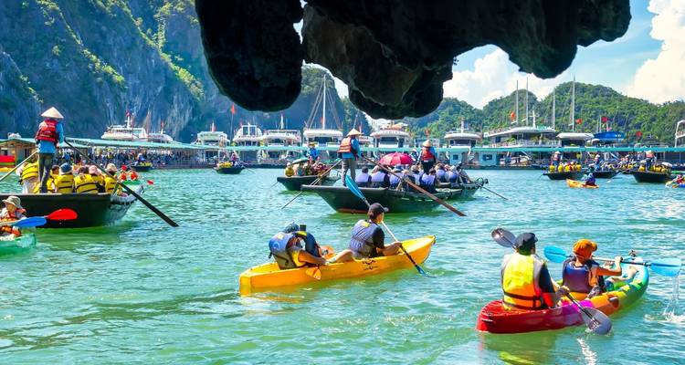 Los kayaks y botes de remos coloridos se amontonan en las aguas esmeralda de la bahía de Halong bajo los acantilados de piedra caliza que se alzan imponentes.