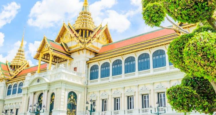 Edificio del Gran Palacio blanco brillante y dorado con topiario cuidadosamente recortado contra un cielo azul en Bangkok.