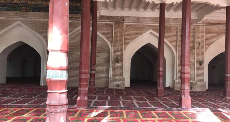 Interior of a mosque with tall red columns and decorative carpets.