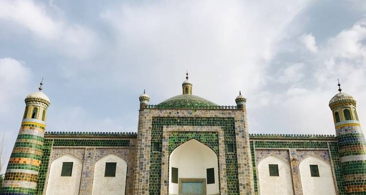 A grand mosque with green-tiled domes against a cloudy sky.