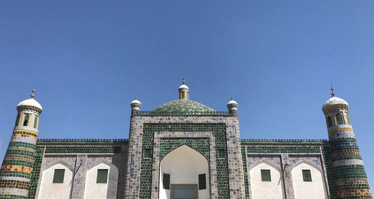 A mosque with multiple domes and intricate tile work under a clear blue sky.