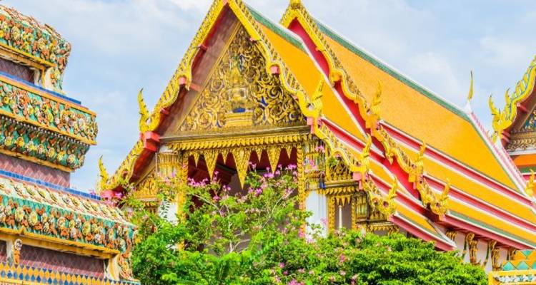 Leuchtend farbige, kunstvoll verzierte Dächer und Giebel von thailändischen Tempeln heben sich vor einem hellblauen Himmel ab.