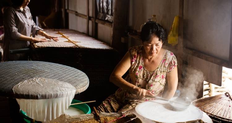 Vietnamese women making rice paper over steam in a traditional workshop.