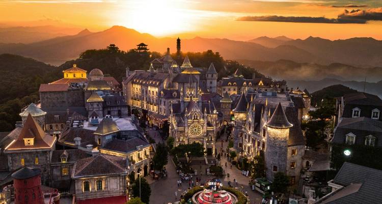 Aerial sunset view of French-style Ba Na Hills village with mountains in the background.