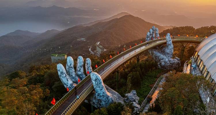Iconic Golden Bridge held by giant stone hands spanning a forested valley at sunrise.