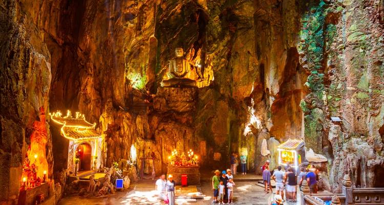Illuminated shrine and statue inside a colorful limestone cave with visitors exploring.