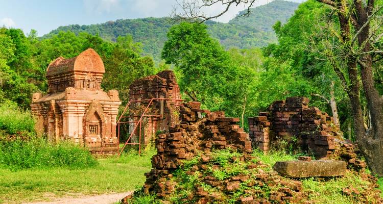 Scattered brick temple ruins overgrown with vegetation in a lush forest setting.