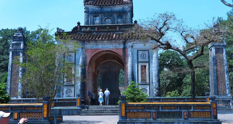 Visitors standing at the entrance of an ornate tomb gate surrounded by trees in Hue.
