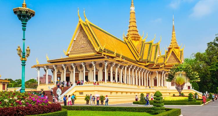 Sierlijke gouden hal van het Koninklijk Paleis in Phnom Penh met tuinen en groepen bezoekers.