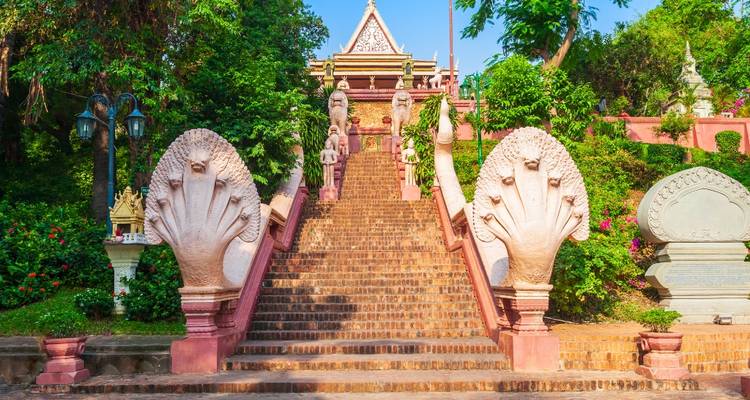 Bakstenen trap met roze naga-beelden met meerdere koppen aan beide zijden die naar een tempel op een heuvel in het groen leidt.