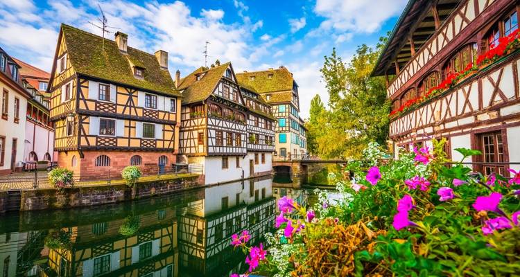 Half-timbered houses of Strasbourg’s Petite France mirrored in a tranquil canal adorned with vibrant flowers.