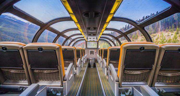 Interior of a glass-domed observation rail car offering panoramic mountain views