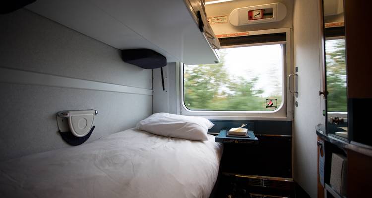Compact single sleeper cabin on a train with a window view of blurred greenery
