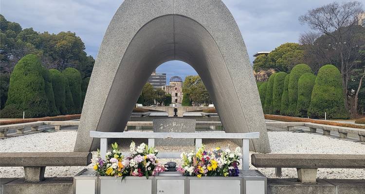 Gedenkdenkmal mit Blumen und Bäumen im Hintergrund.