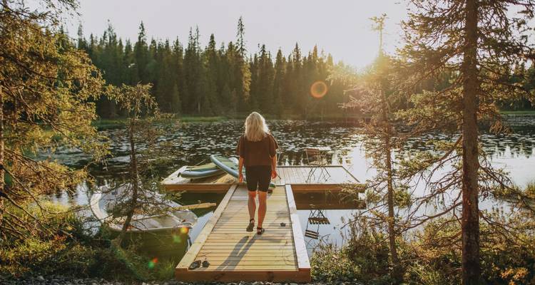 Eine Frau, die bei Sonnenuntergang auf einem Steg in Richtung eines Sees geht.