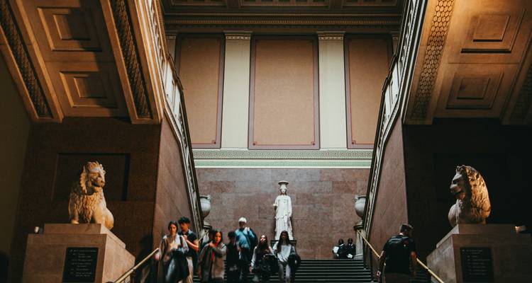 Des personnes marchant à l'intérieur d'un grand musée avec des statues.