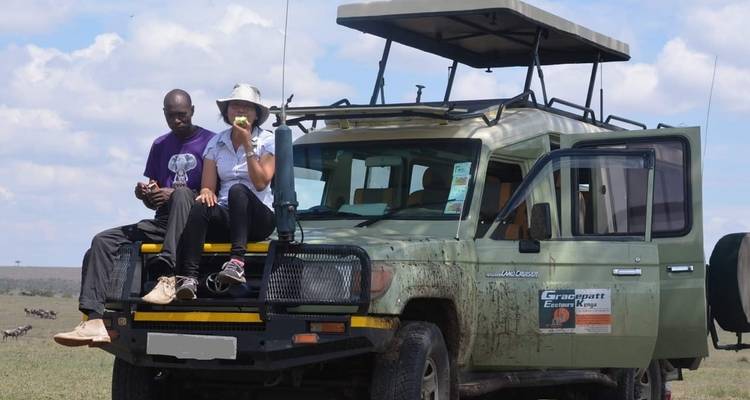 Zwei Personen sitzen auf der Motorhaube eines Safari-Fahrzeugs.