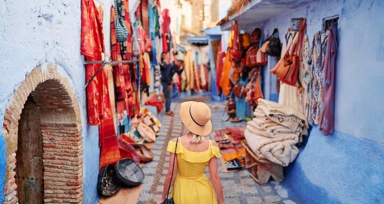 Woman walking through a colorful market street lined with blue buildings.
