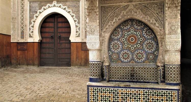 Intricately designed mosaic fountain next to a carved wooden door.