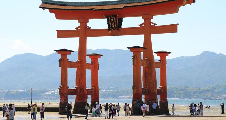 Berühmtes Torii-Tor am Itsukushima-Schrein mit Menschen, die in der Nähe spazieren gehen.