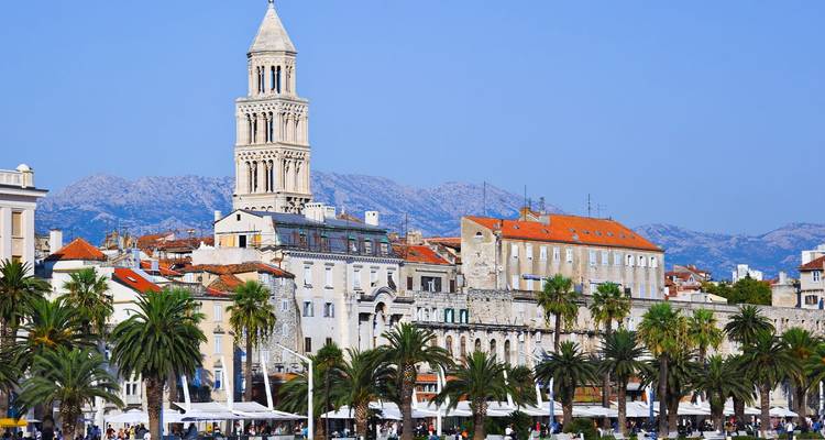Seafront promenade of Split lined with palm trees and the bell tower of St. Domnius against clear blue sky.