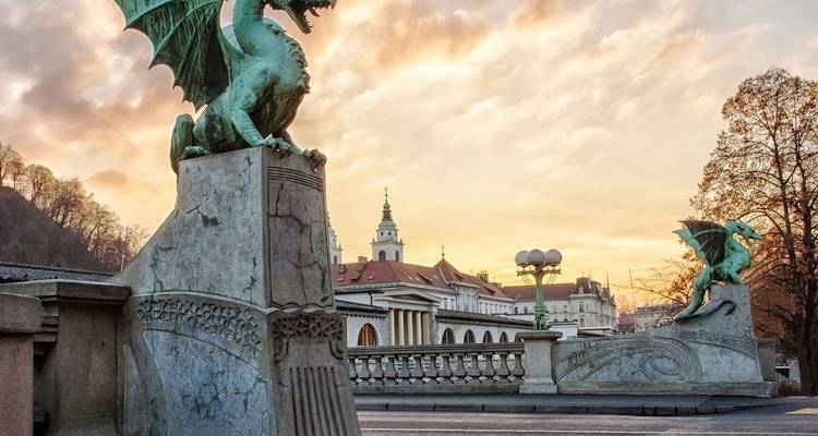 Green dragon statues guard Ljubljana’s Dragon Bridge at sunrise with historic skyline softly lit behind.