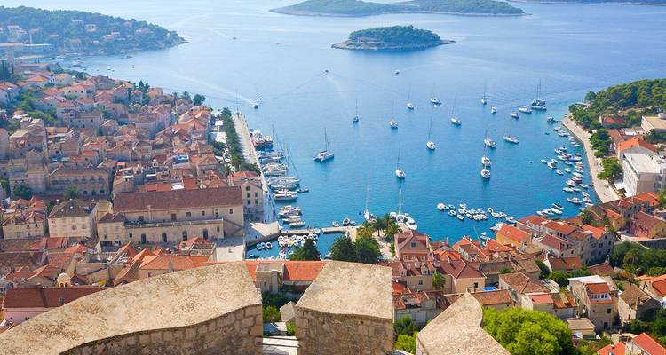 Hilltop vista over Hvar harbour with yachts anchored in blue bay dotted by small forested islands.