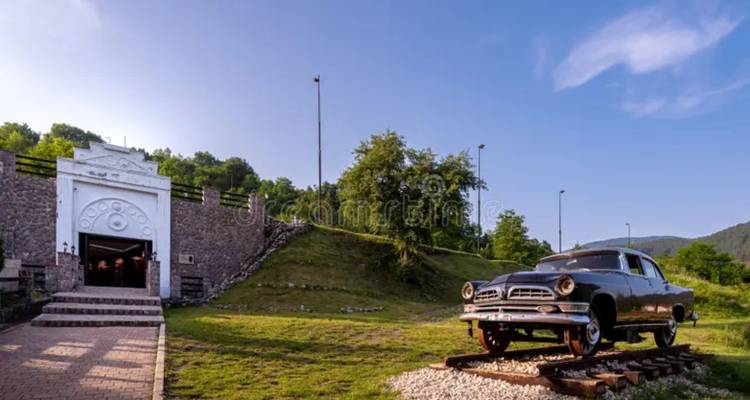 Voiture noire vintage montée sur des rails courts à côté de l'entrée d'un tunnel en pierre au milieu de collines herbeuses.