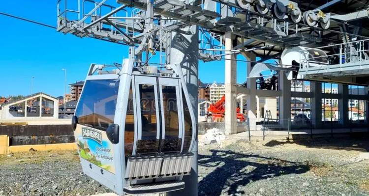 Gros plan d'une cabine de télécabine moderne sur une ligne de téléphérique nouvellement construite sur fond de ciel bleu éclatant et d'immeubles d'habitation.