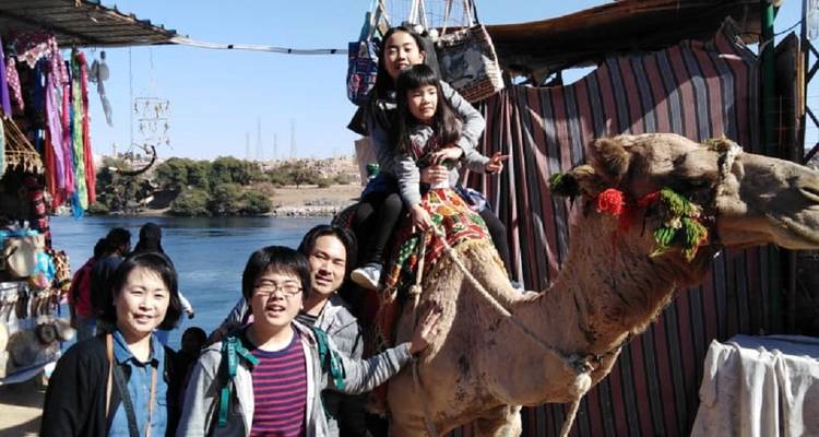 Familie posiert mit einem Kamel bei einem Markt am Flussufer in Ägypten.