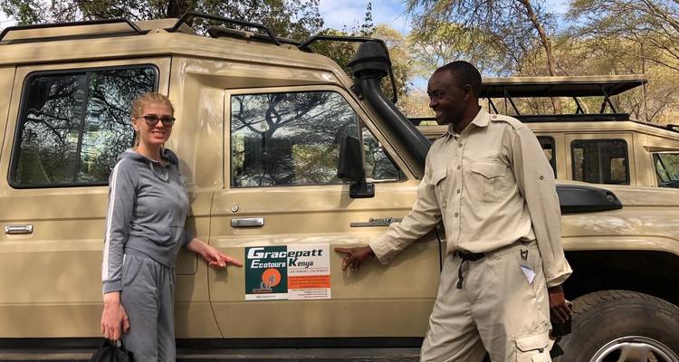 Zwei Personen stehen neben einem Safari-Fahrzeug in einer Parkumgebung.