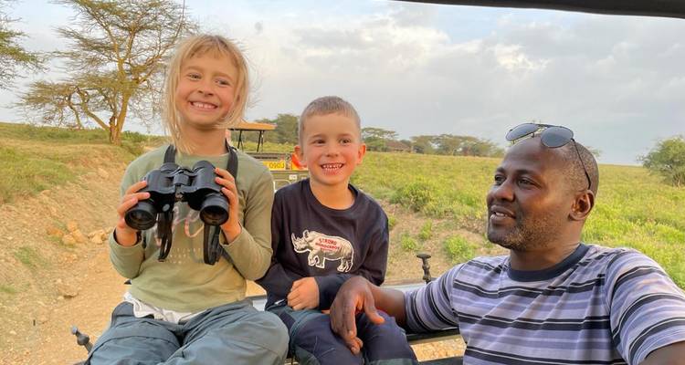 Guide with two children holding binoculars on a safari vehicle.