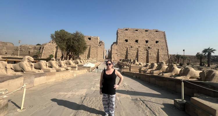 Una mujer se encuentra con confianza en la avenida de las esfinges del Templo de Karnak bajo un cielo sin nubes.