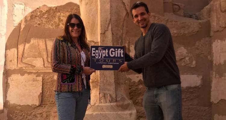 Couple with a tour sign in front of Egyptian carvings.