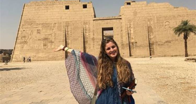 Smiling woman in front of an ancient temple entrance.
