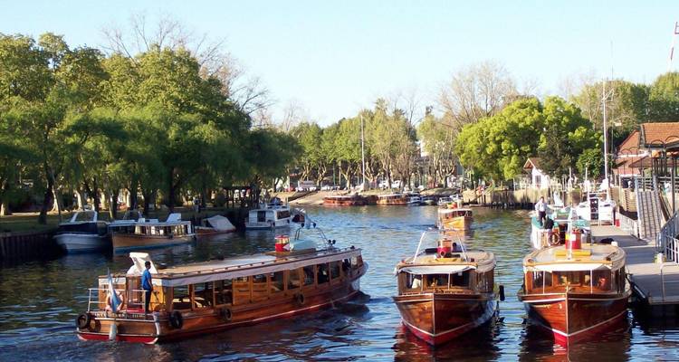 Holzboote auf einem Fluss mit Bäumen und einem Steg im Hintergrund.