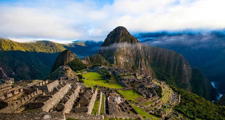 Ruinen von Machu Picchu mit einem Berg und Wolken im Hintergrund.