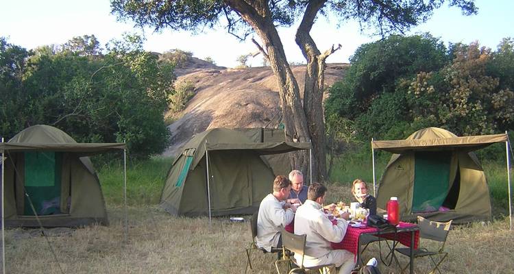 Menschen, die an einem Tisch vor Zelten auf einem Campingplatz sitzen.