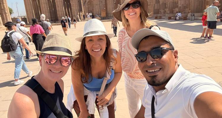 Vier bezoekers die poseren in de heldere binnenplaats van de Luxor Tempel met hoeden en zonnebrillen op.