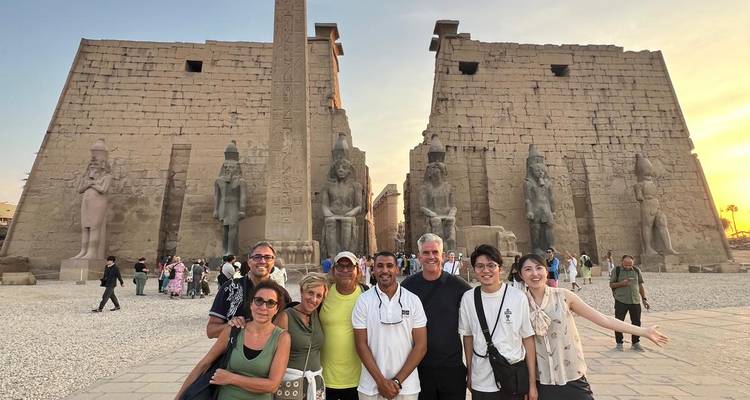 Grote groep die staat voor de monumentale pylonen en obelisk van de Luxor Tempel bij zonsondergang.