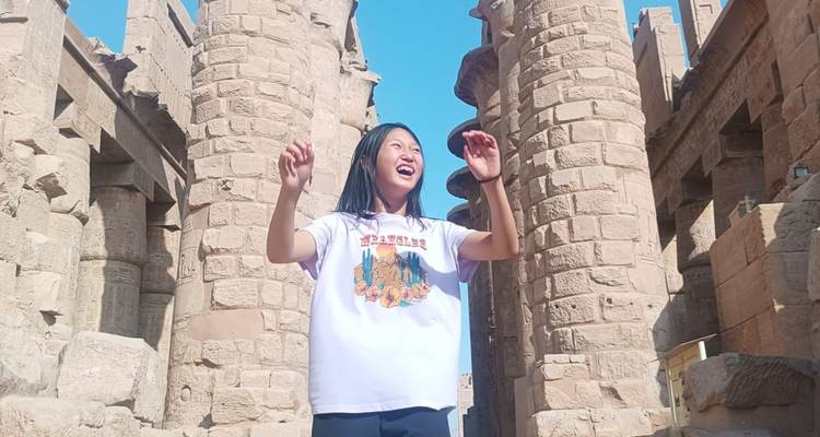 Jonge vrouw lachend tussen hoge zandstenen zuilen van de Karnak Tempel met blauwe lucht erboven.